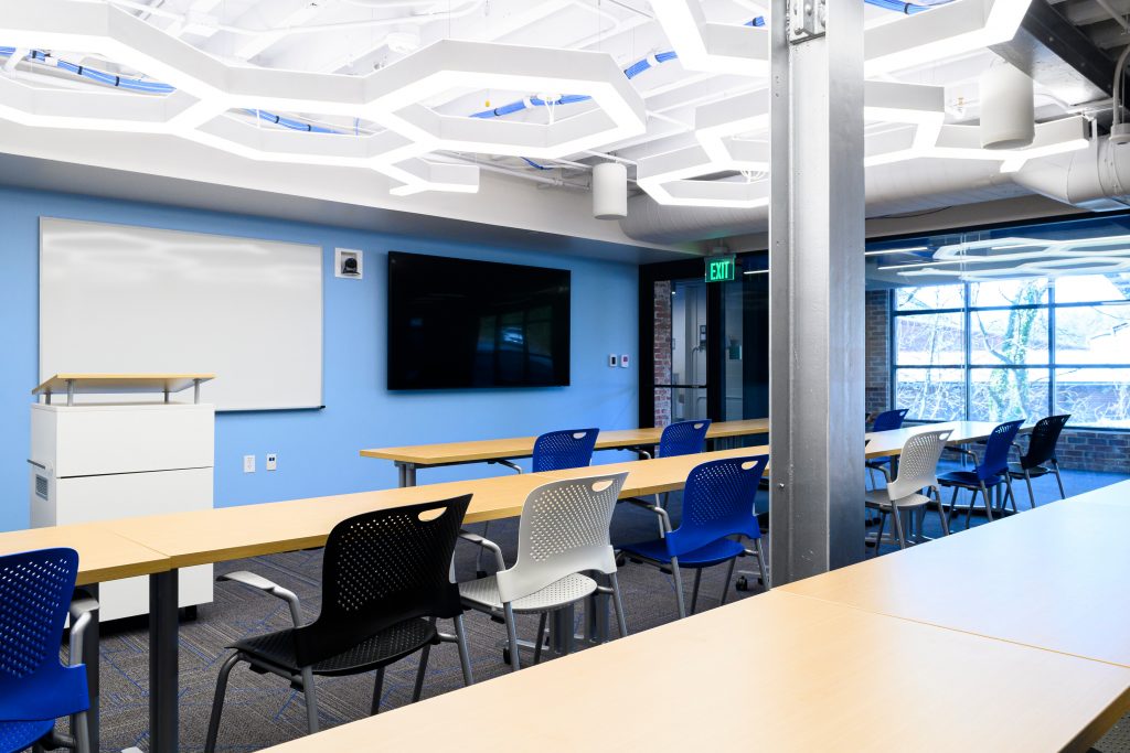 Classroom space featuring blue accent wall; black, white and blue chairs; and unique honeycomb lighting.