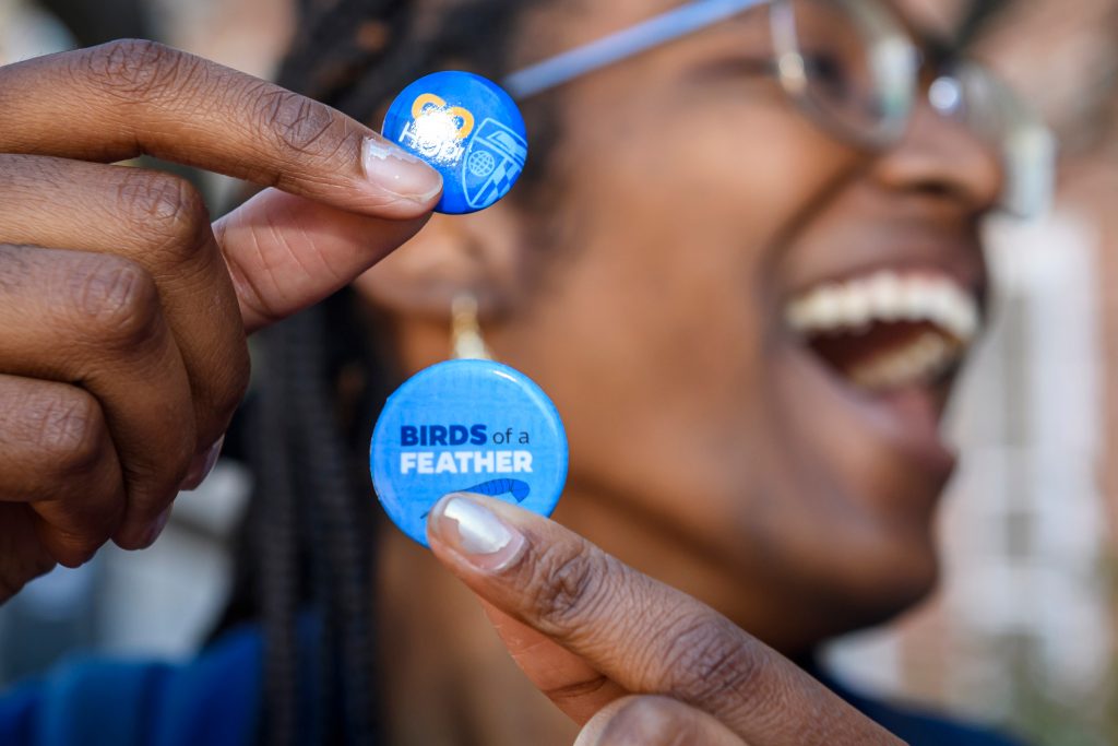 Promotional pin that reads "Birds of a Feather" with feather background