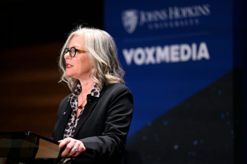 Woman speaking at podium with banner in the background that includes Johns Hopkins University logo next to Vox Media logo.