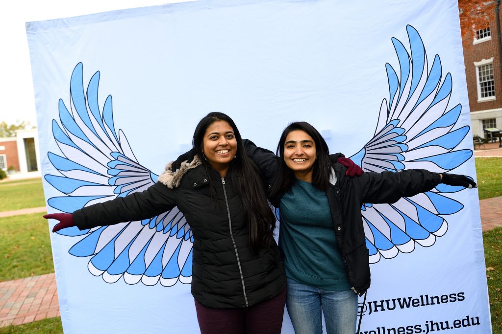 Two students posing in front of a background featuring blue jay wings