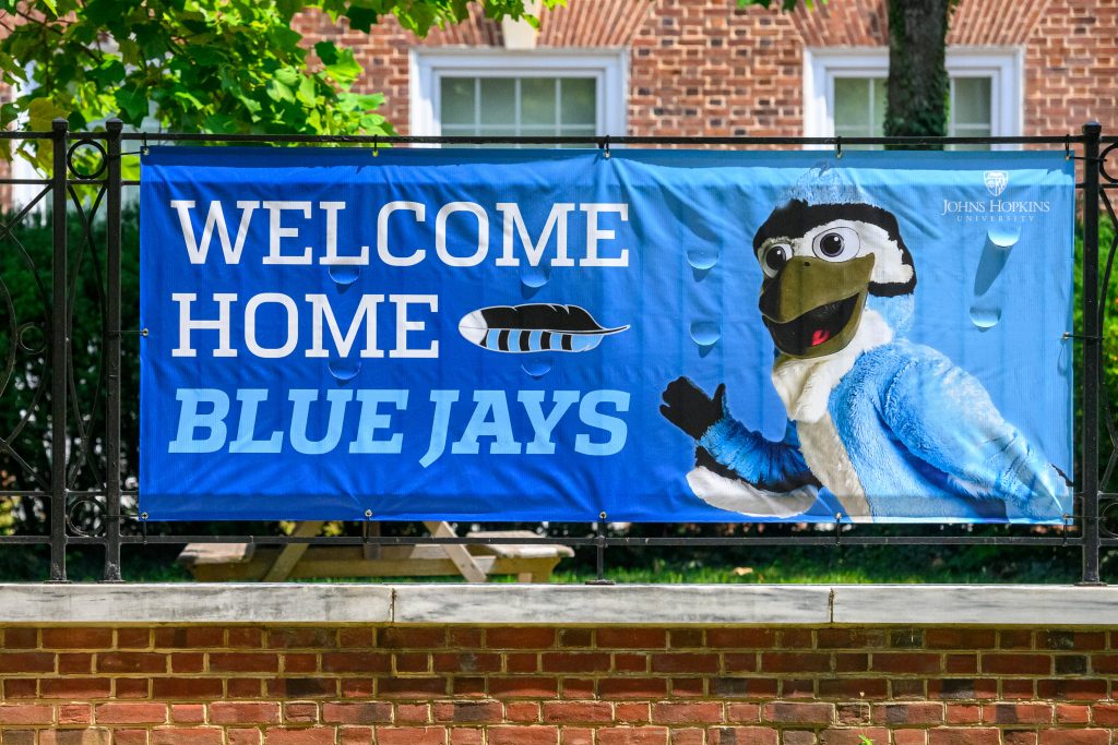 Large banner tied to fence with Blue Jay mascot photo and message that reads "Welcome Hopkins Blue Jays"