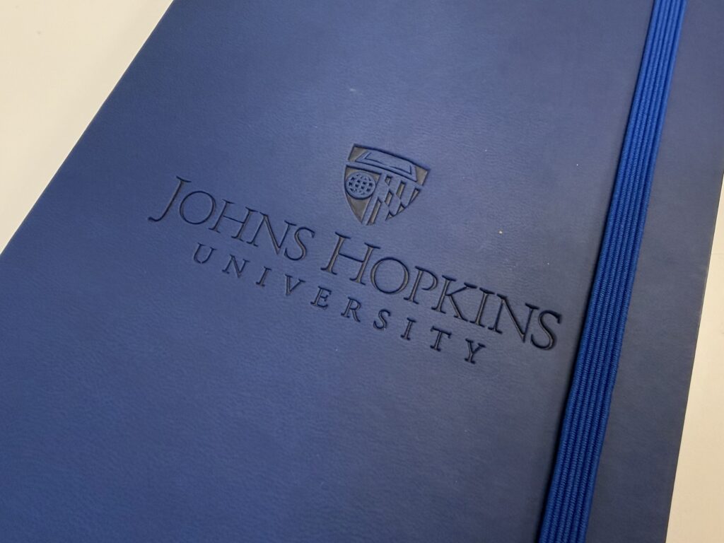 Johns Hopkins University blue logo debossed on a notebook